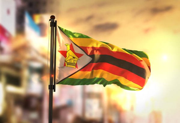 Zimbabwe Flag Against City Blurred Background At Sunrise Backlight